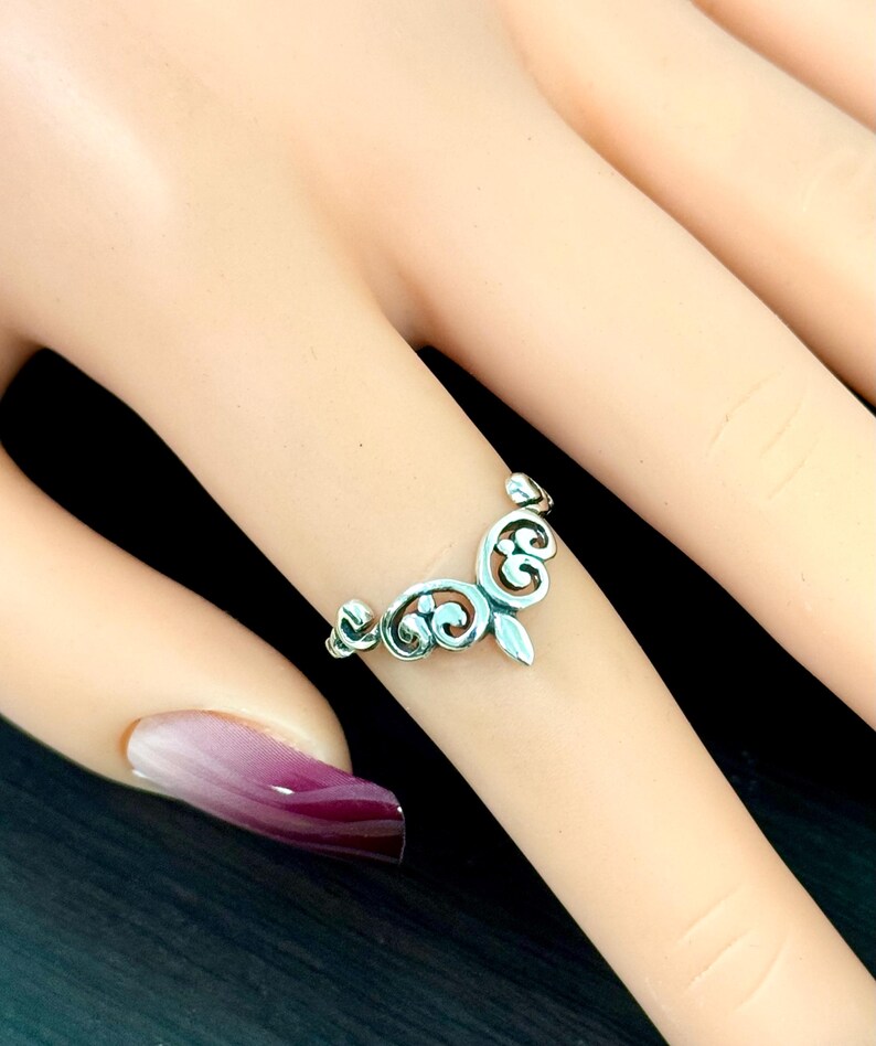May include: A silver ring with a delicate, ornate design. The ring is shaped like a crown with a pointed tip.