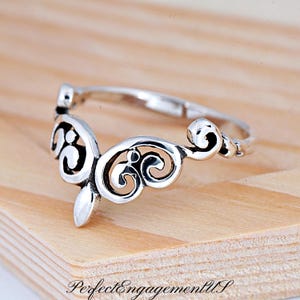 May include: A silver ring with a delicate, ornate design. The ring features a swirling, openwork pattern that resembles a crown or a stylized flower.