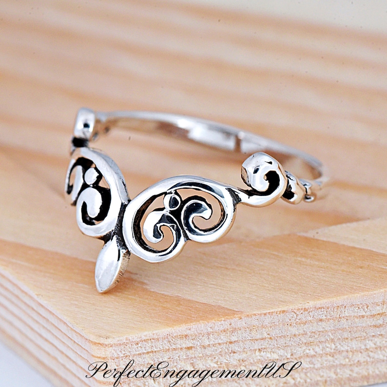 May include: A silver ring with a delicate, ornate design. The ring features a swirling, openwork pattern that resembles a crown or a stylized flower.