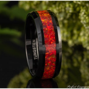 May include: A black tungsten ring with a red and orange opal inlay. The ring is engraved with the word "TUNGSTEN".