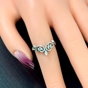 May include: A silver filigree ring with a delicate, ornate design. The ring is shown on a model's finger.