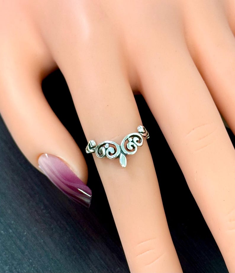 May include: A silver filigree ring with a delicate, ornate design. The ring is shown on a model's finger.
