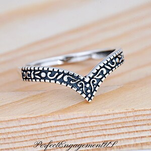 May include: A silver ring with a V-shaped band and an intricate black floral design.