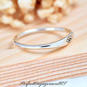 May include: A silver ring with a simple design featuring a small eye symbol on the band.