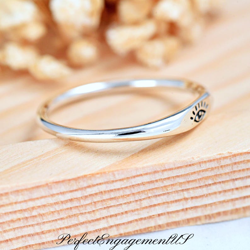 May include: A silver ring with a simple design featuring a small eye symbol on the band.