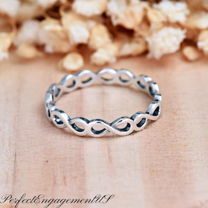 May include: A silver infinity ring with a delicate, intertwined design. The ring is simple and elegant, making it a perfect choice for everyday wear.