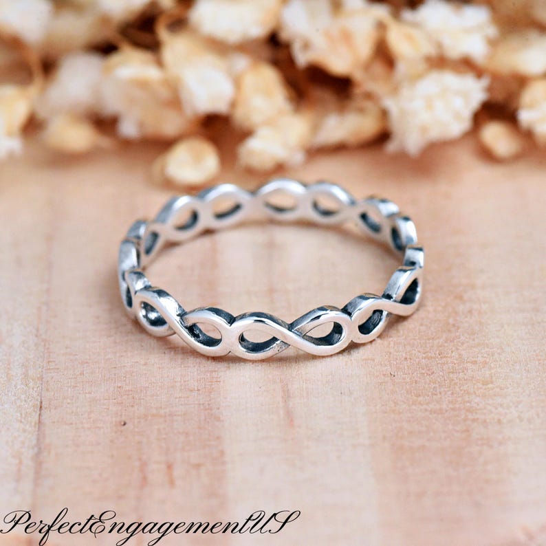 May include: A silver infinity ring with a delicate, intertwined design. The ring is simple and elegant, making it a perfect choice for everyday wear.