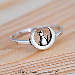 May include: A silver ring with a crescent moon design featuring a small cat sitting on the moon.