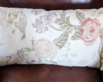 May include: A cream-colored pillow with a floral pattern featuring pink and brown roses, leaves, and sprigs. The pillow has a ruffled edge.