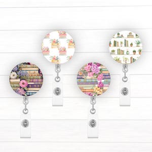 May include: Four different patterned retractable badge holders with a white background. The patterns feature stacks of books with flowers and plants.