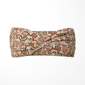 May include: A light green fabric headband featuring a twisted front design and a repeating pattern of framed illustrations including turkeys, pumpkins, slices of pie, and autumn leaves in shades of orange, brown, and red across the entire surface.