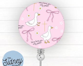 May include: A pink retractable badge reel with a repeating pattern of white geese, pink bows, gold crosses, white daisies, and stars. The text "Jesus loves you, silly goose!" is also featured. The reel has a silver clip and a clear plastic strap.