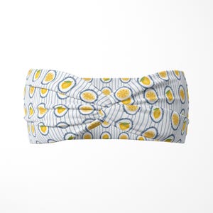 May include: A white headband with a blue striped pattern and a repeating design of lemons. The lemons are yellow with green leaves and are set within a blue scalloped border.