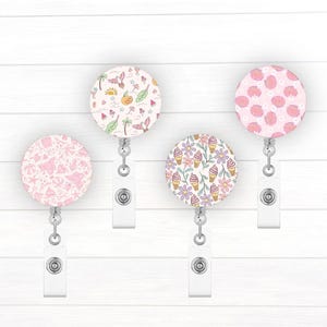 May include: Four different patterned retractable badge holders. The patterns include pink seashells, pink flowers with ice cream cones, pink flamingos and palm trees, and pink and white seashells.