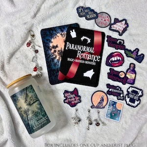 May include: A frosted glass cup with a bamboo lid, a rectangular book-style box labeled Paranormal Romance, and various stickers and charms featuring vampire, werewolf, and moon themes. The box text reads Paranormal Romance Magic Mayhem Monsters.