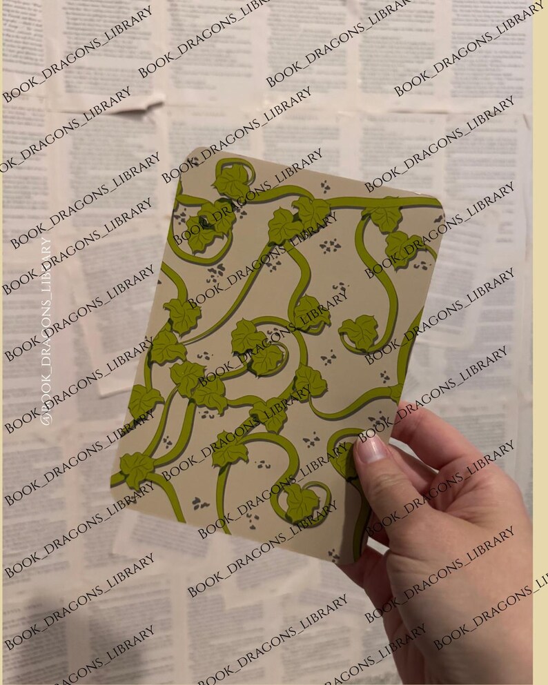 Pu&ograve; includere: Una carta rettangolare con sfondo beige e motivo a vite verde con foglie. La carta &egrave; tenuta in mano su uno sfondo di pagine di vecchi libri. Il testo "BOOK_DRAGONS_LIBRARY" &egrave; stampato sulla carta e sullo sfondo.