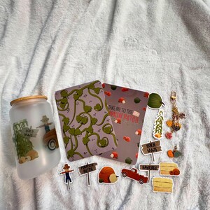 May include: A frosted glass tumbler with a bamboo lid featuring a scarecrow and truck graphic, two rectangular cards with vine and pumpkin patterns, and various die-cut stickers including a scarecrow, signs, pumpkins, and a metal keychain.