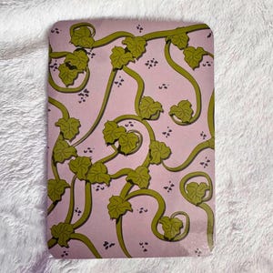 May include: A rectangular sheet with a light purple background featuring a repeating pattern of winding olive green vines and pointed leaves. Small clusters of dark purple dots are scattered throughout the design, creating a botanical motif.