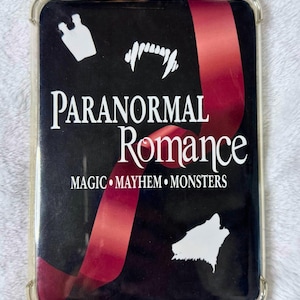 May include: A rectangular clear phone case featuring a black insert with a red ribbon graphic. The text reads PARANORMAL ROMANCE and MAGIC MAYHEM MONSTERS. White silhouettes of vampire fangs, a potion bottle, and a howling wolf are visible.