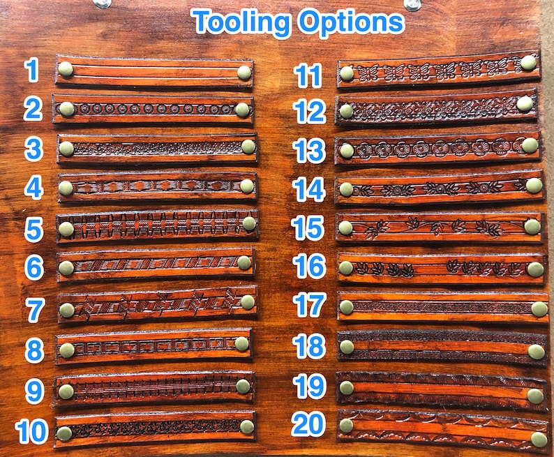 May include: A wooden display board with the text "Tooling Options" features twenty samples of tooled leather straps. Each strap is a different design, ranging from simple lines to intricate floral patterns. The straps are secured with brass rivets.