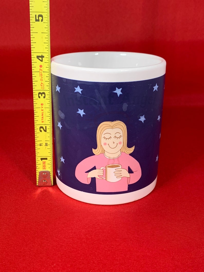 K&ouml;nnte beinhalten: Eine wei&szlig;e Keramiktasse mit blauem Hintergrund und wei&szlig;en Sternen. Eine Comic-Frau mit blonden Haaren h&auml;lt eine Tasse Kaffee und l&auml;chelt. Der Text auf der Tasse lautet "Ich sage nicht, dass ich faul bin, aber ich sage auch nicht, dass ich nicht faul bin."