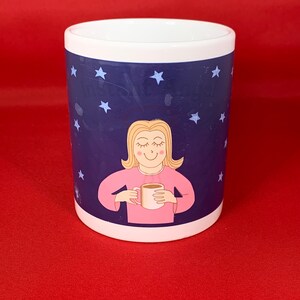 K&ouml;nnte beinhalten: Wei&szlig;e Keramiktasse mit einem blauen und wei&szlig;en Sternenhimmel-Design. Eine Comic-Frau mit blonden Haaren h&auml;lt eine wei&szlig;e Tasse mit einem braunen Getr&auml;nk darin.