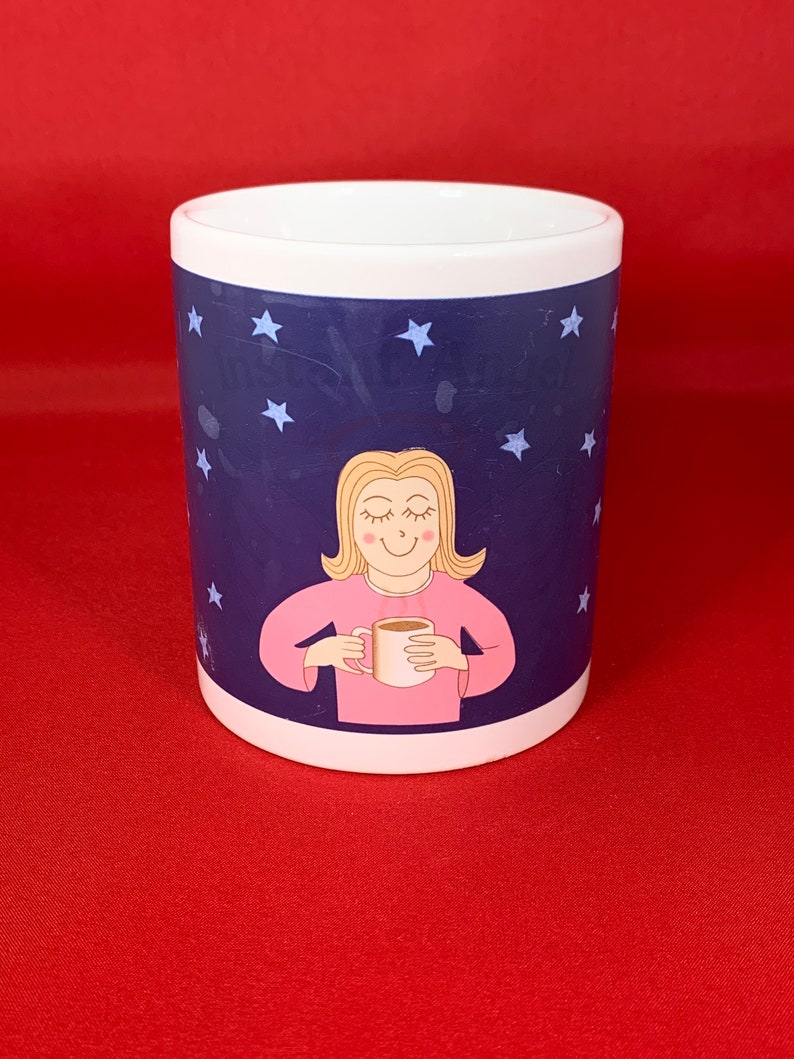K&ouml;nnte beinhalten: Wei&szlig;e Keramiktasse mit einem blauen und wei&szlig;en Sternenhimmel-Design. Eine Comic-Frau mit blonden Haaren h&auml;lt eine wei&szlig;e Tasse mit einem braunen Getr&auml;nk darin.