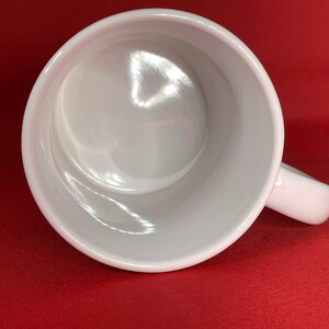 K&ouml;nnte beinhalten: Eine wei&szlig;e Keramiktasse mit glattem, gl&auml;nzendem Innenraum. Die Tasse hat einen Henkel und ist leer.