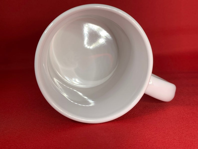 K&ouml;nnte beinhalten: Eine wei&szlig;e Keramiktasse mit glattem, gl&auml;nzendem Innenraum. Die Tasse hat einen Henkel und ist leer.
