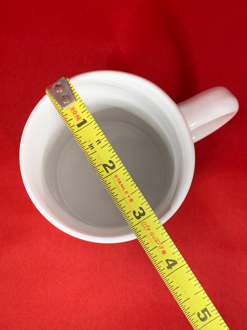 K&ouml;nnte beinhalten: Wei&szlig;e Keramiktasse mit einem gelben Ma&szlig;band darum gewickelt. Das Band misst 10 cm.