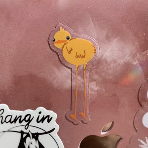 May include: A yellow cartoon bird with long legs and a small beak. The bird is standing on a pink surface.
