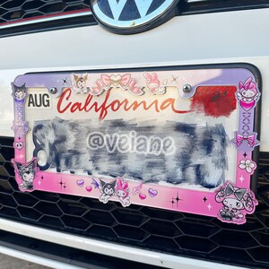 May include: A decorative license plate frame with a pink and purple border. The frame features cartoon characters, bows, and the word "California" in red script. The license plate itself is partially obscured.