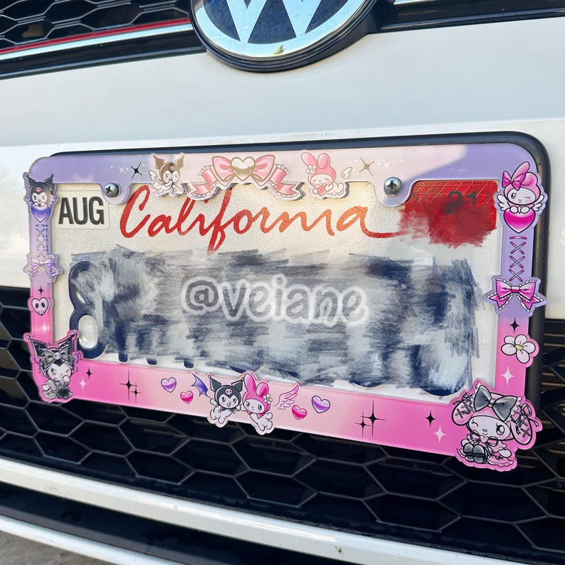 May include: A decorative license plate frame with a pink and purple border. The frame features cartoon characters, bows, and the word "California" in red script. The license plate itself is partially obscured.