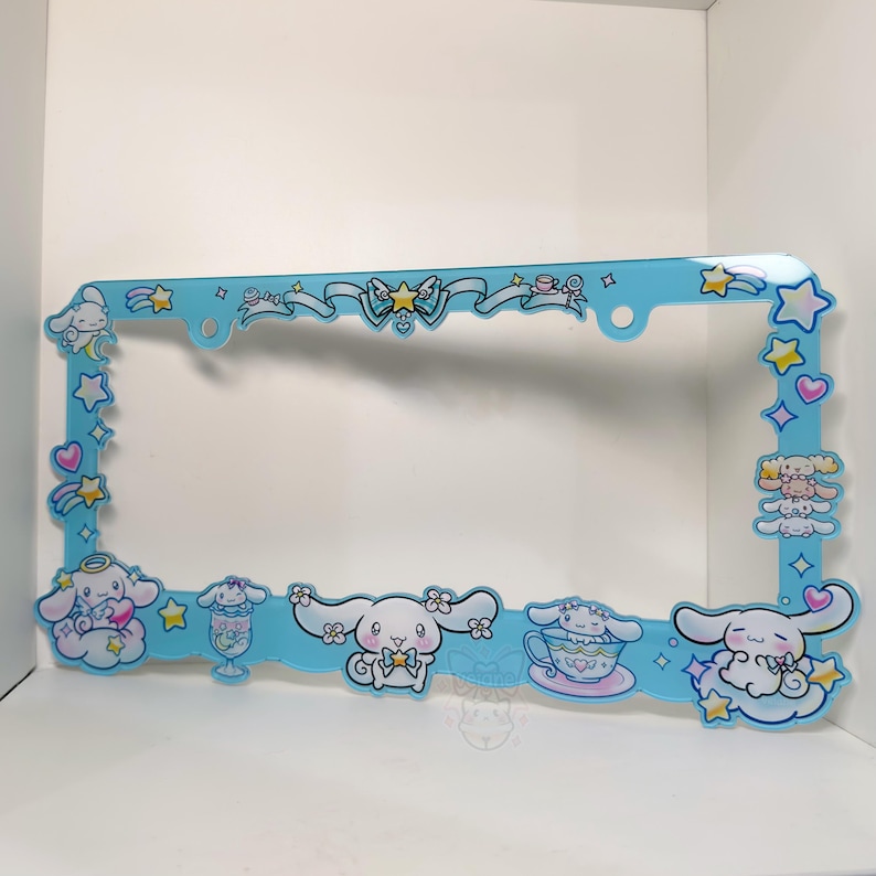 Puede incluir: Un marco de matr&iacute;cula azul claro con personajes de dibujos animados, estrellas, corazones y lazos. El marco tiene forma rectangular con esquinas redondeadas y est&aacute; decorado con varias figuras de dibujos animados.