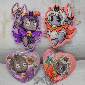 May include: Four colorful pins featuring a cartoon character with horns, a bell, and a crown. The character is holding a sword, an axe, and a bell. The pins are heart-shaped and have glitter on them. The text on the pins reads "Join my cult?"
