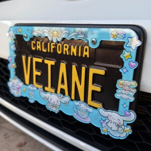 Puede incluir: Una placa de matr&iacute;cula de California con el texto "VETANE" en letras amarillas sobre un fondo negro. La placa est&aacute; enmarcada por un borde azul claro con personajes de dibujos animados, estrellas y corazones.