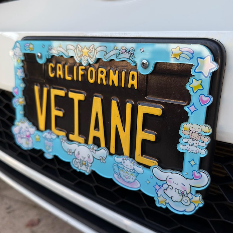 Puede incluir: Una placa de matr&iacute;cula de California con el texto "VETANE" en letras amarillas sobre un fondo negro. La placa est&aacute; enmarcada por un borde azul claro con personajes de dibujos animados, estrellas y corazones.