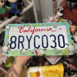 May include: California license plate with the text "California" in red script. The plate has the number "8RYCO30" in dark blue. The border is light blue with cartoon characters and decorative elements.
