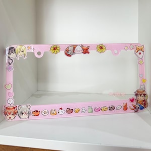 May include: Pink plastic license plate frame with a variety of cartoon animal stickers, including cats, dogs, and a chicken. The frame also features a few anime characters and the text "@veiane".