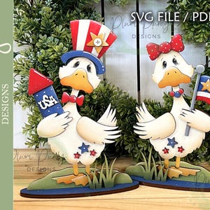 Peut inclure: Deux figurines de canards en bois sur le thème patriotique. L'un tient une fusée bleue avec "USA", l'autre un petit drapeau américain. Les deux canards ont des accents rouges, blancs et bleus, et se tiennent sur une base verte.
