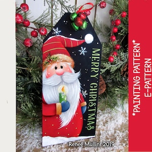 May include: A painted wooden Christmas ornament featuring a cartoon Santa Claus holding a candle. The ornament is black with white snowflakes and the text "Merry Christmas".
