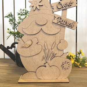 K&ouml;nnte beinhalten: Unbemalte Holzfigur eines Zwergs mit einer Blume auf seinem Hut, der einen Vogel in der Hand h&auml;lt. Der Zwerg steht neben einem Schild mit der Aufschrift "Crow Patrol".