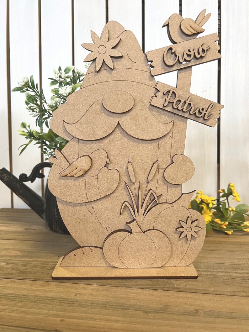 K&ouml;nnte beinhalten: Unbemalte Holzfigur eines Zwergs mit einer Blume auf seinem Hut, der einen Vogel in der Hand h&auml;lt. Der Zwerg steht neben einem Schild mit der Aufschrift "Crow Patrol".