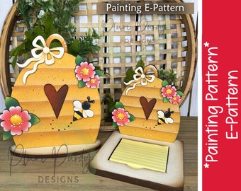 May include: A wooden beehive-shaped notepad holder with a heart cutout, painted in yellow, brown, and pink with a bee and flowers. The holder is on a wooden base and has a yellow notepad inside.