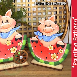 Könnte beinhalten: Zwei bemalte Holzschweinefiguren, die in Wassermelonenstücken auf Rädern sitzen. Die Schweine tragen blaue und weiße Bandanas. Die Wassermelonenstücke sind rot mit schwarzen Kernen und grünen Schalen. Die Räder sind braun mit silbernen Zentren. Der Hintergrund ist ein Weidenkorb.