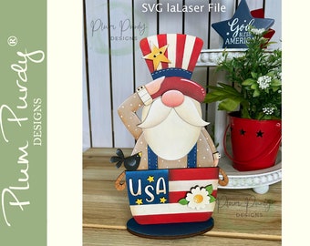 May include: Patriotic gnome figurine with a red, white and blue hat, holding a small bird in a bucket with a USA flag design. The gnome is wearing a red, white and blue hat with a star on top. The gnome is holding a small bird in a bucket with a USA flag design. The bucket is painted red, white and blue with stars and the word "USA" in white letters. The gnome is standing on a wooden base.