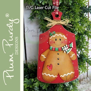 Puede incluir: Adorno navideño de madera con forma de tabla de cortar, con un diseño de hombre de jengibre. El adorno es rojo con lunares blancos y un hombre de jengibre con una bufanda verde y roja. El texto "SVG Laser Cut File" es visible.