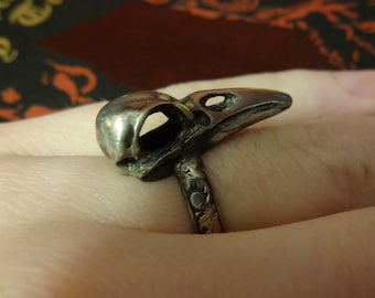May include: A silver ring with a detailed bird skull design. The ring band is also silver and has a decorative pattern.