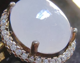 May include: A white oval gemstone ring with a silver band and a row of small clear stones around the setting.