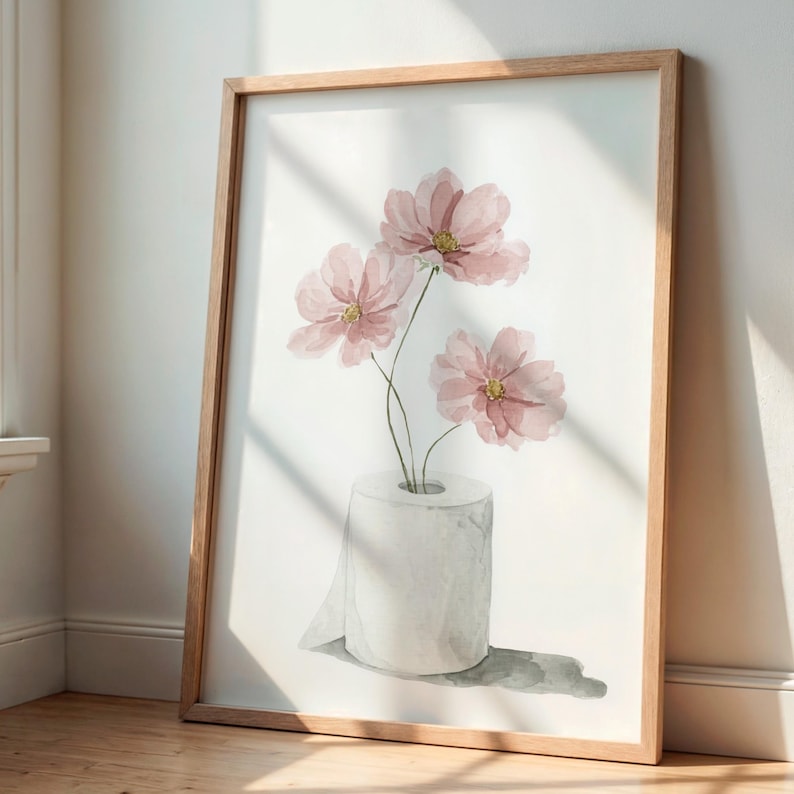 Puede incluir: Impresi&oacute;n art&iacute;stica en acuarela con tres flores rosas en un rollo de papel higi&eacute;nico. Las flores tienen centros amarillos y est&aacute;n sobre un fondo blanco. La obra de arte est&aacute; enmarcada en un marco de madera marr&oacute;n claro.